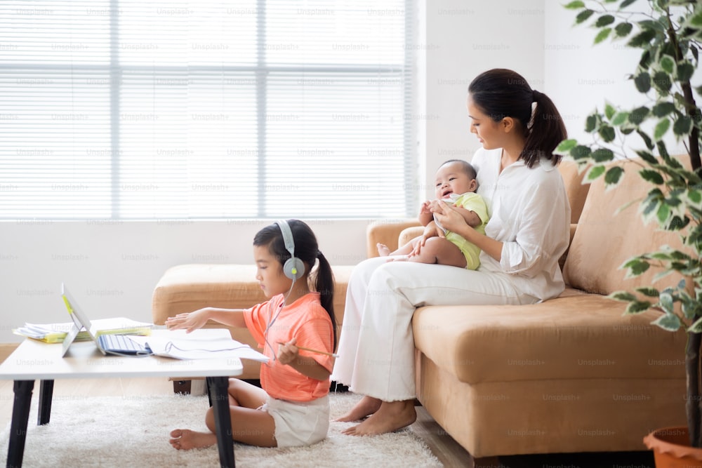 Her daughter is studying online at home. Her mother is with a baby