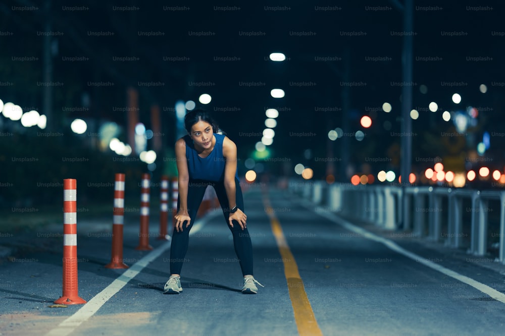 Mujer asiática hace ejercicio practicando correr por la noche. Está cansada.