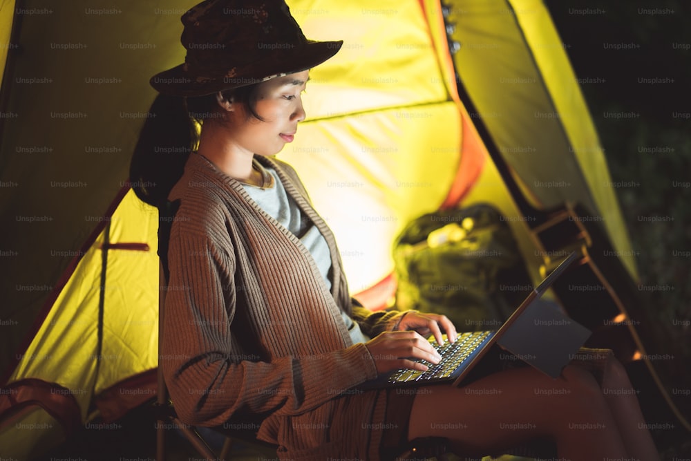 キャンプ中にコンピューターを使ってコミュニケーションをとるアジアの女性