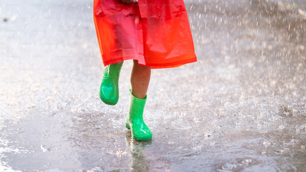 Menina asiática está usando bota verde. Ela está na chuva.