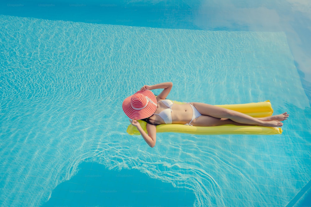 Hermosa mujer, lleva un bikini y duerme en un colchón de aire en la piscina de verano.