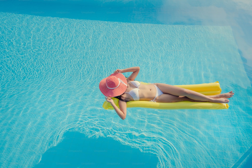 Beautiful woman, she is wearing a bikini and sleeping on an air mattress at the summer pool.