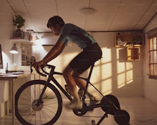 아시아 남자 사이클리스트. 그녀는 집에서 운동하고 있습니다. 트레이너에서 자전거를 타고 온라인 자전거 게임을함으로써 "t"n