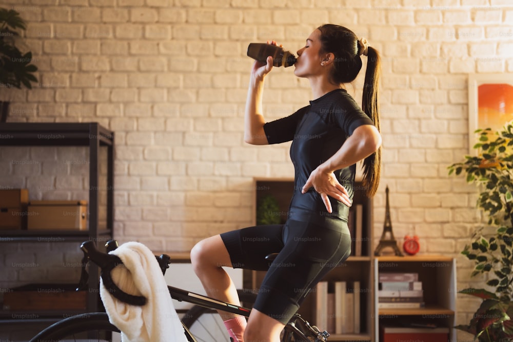 Asian woman cyclist. She is exercising in the house. she drinking water