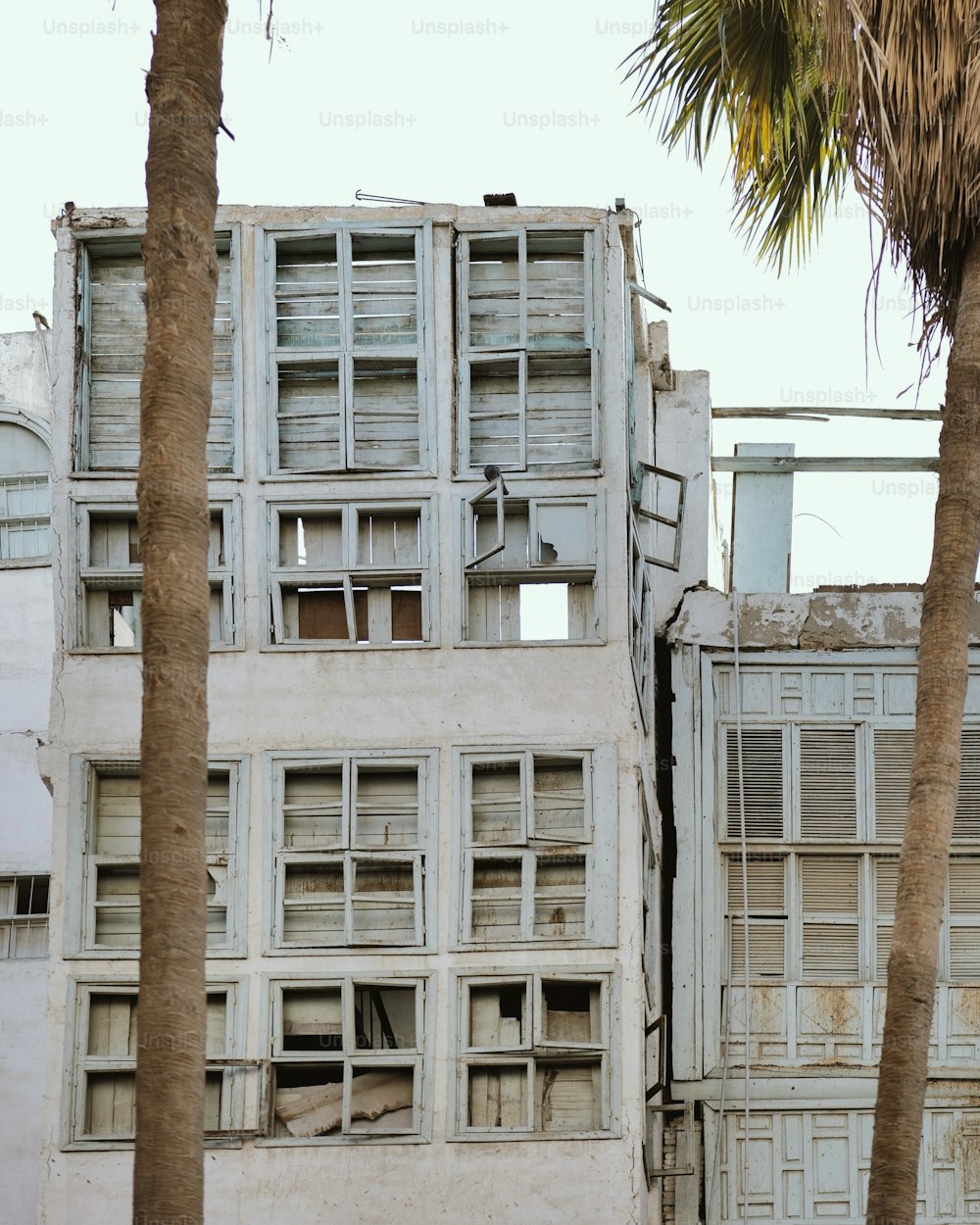 ein altes Gebäude mit zerbrochenen Fenstern und Palmen