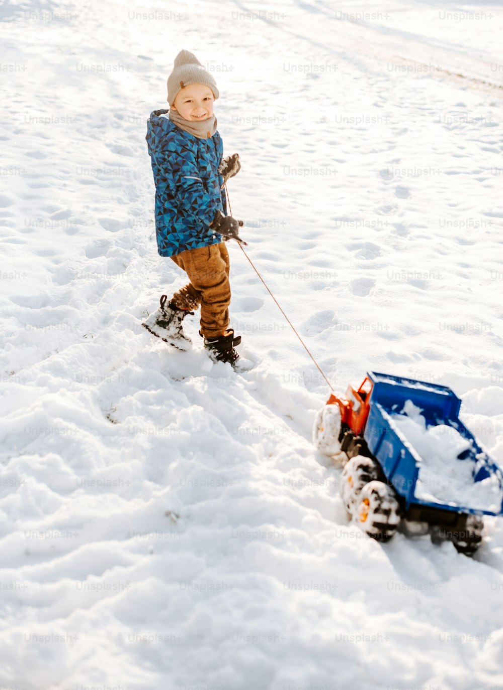 雪の中でおもちゃの車を引っ張る少年