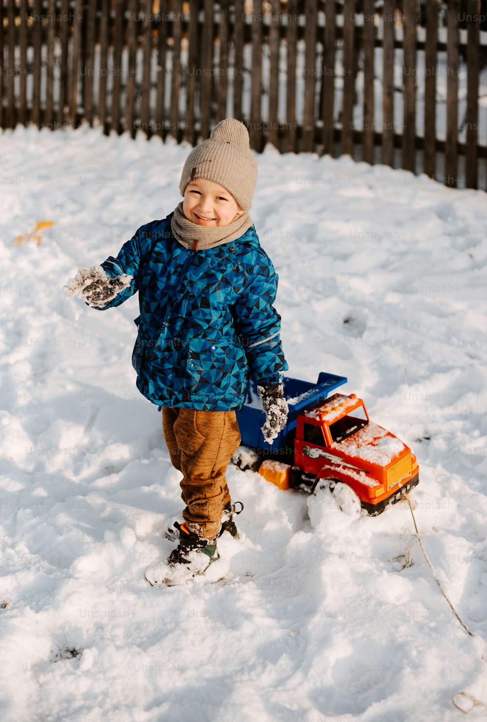 Un ragazzino che gioca nella neve con un camion giocattolo