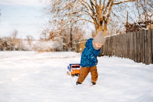 um menino que brinca na neve com um caminhão de brinquedo
