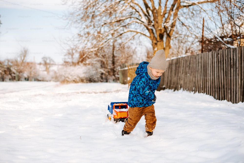 Un giovane ragazzo che gioca nella neve con un camion giocattolo