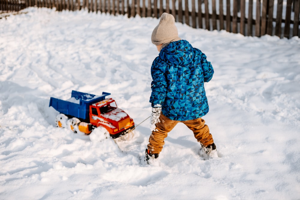 Un ragazzino che gioca nella neve con un camion giocattolo