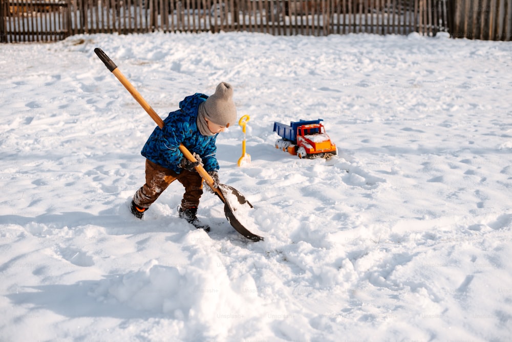 a little boy playing in the snow with a shovel