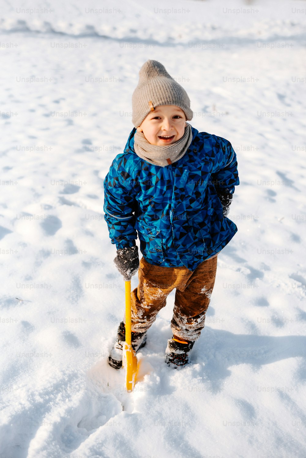 a little boy standing in the snow holding a yellow pole