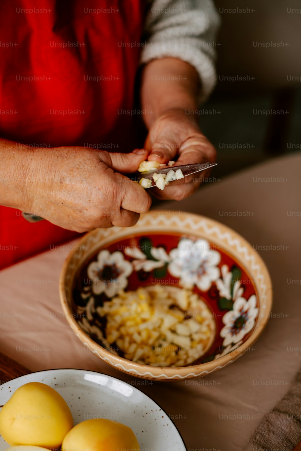 Eine Frau in roter Schürze hält ein Messer und eine Schüssel mit Essen in der Hand
