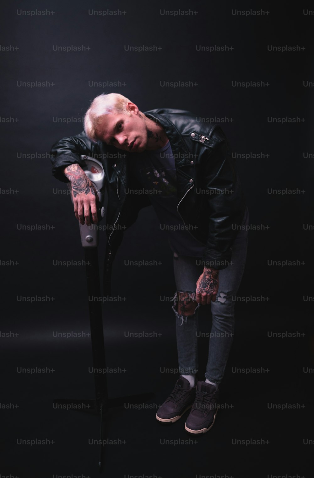 a man in a leather jacket leaning on a pole