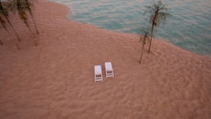 Zwei weiße Liegestühle sitzen auf einem Sandstrand