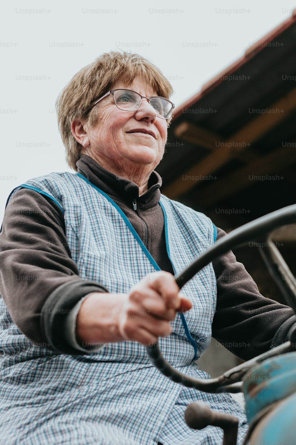 Una mujer mayor conduciendo un tractor con las manos en el volante
