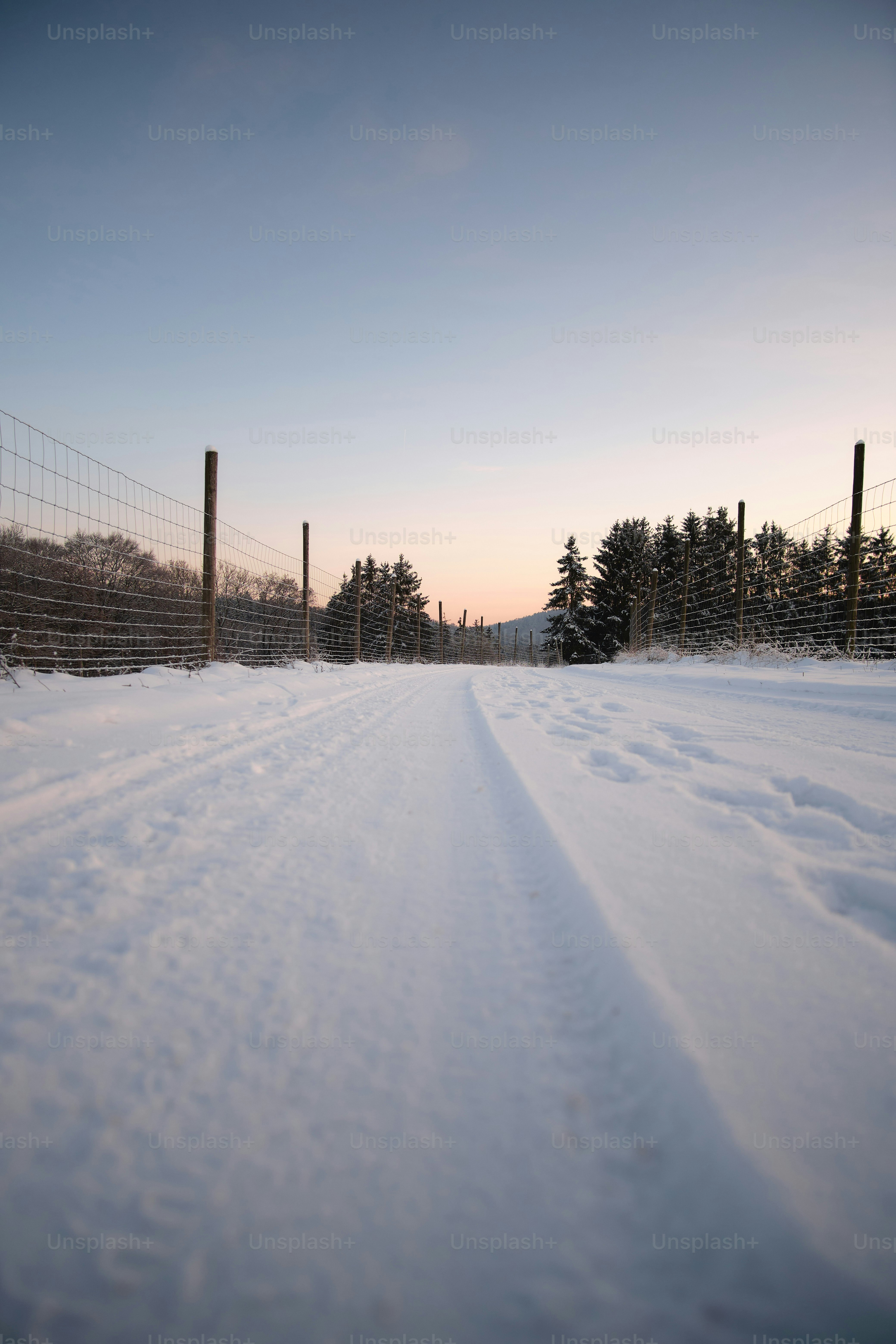 a snow covered road next to a fence