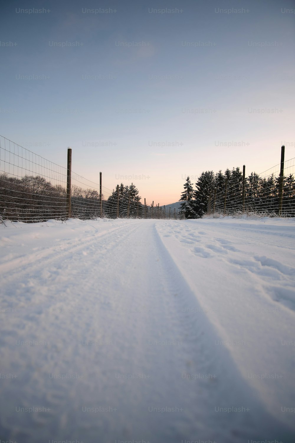 a snow covered road next to a fence