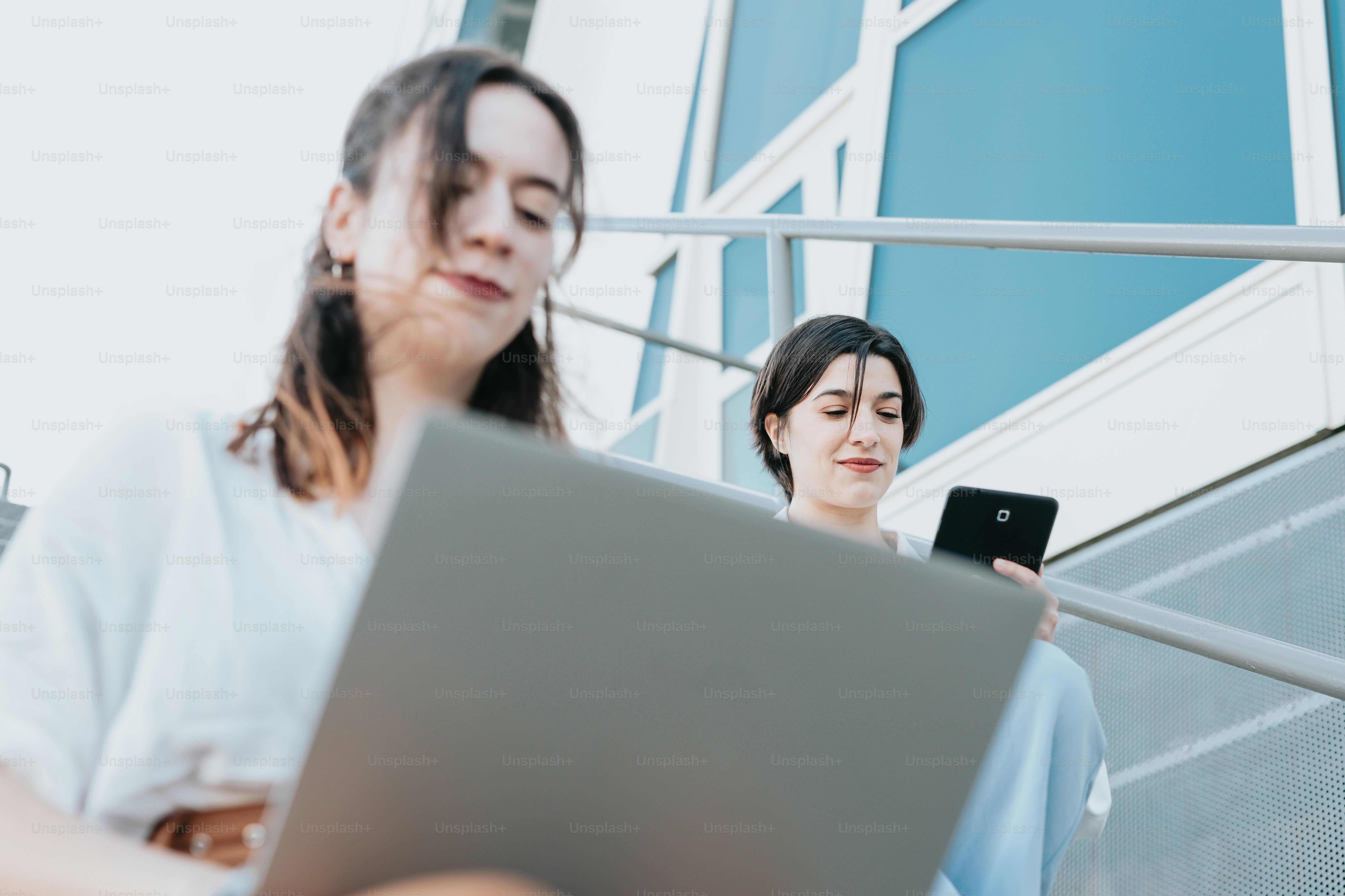 Dos mujeres sentadas en escalones mirando una computadora portátil