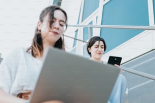 duas mulheres sentadas nos degraus olhando para um laptop