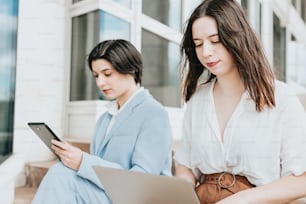 Due donne sedute sui gradini che guardano un tablet
