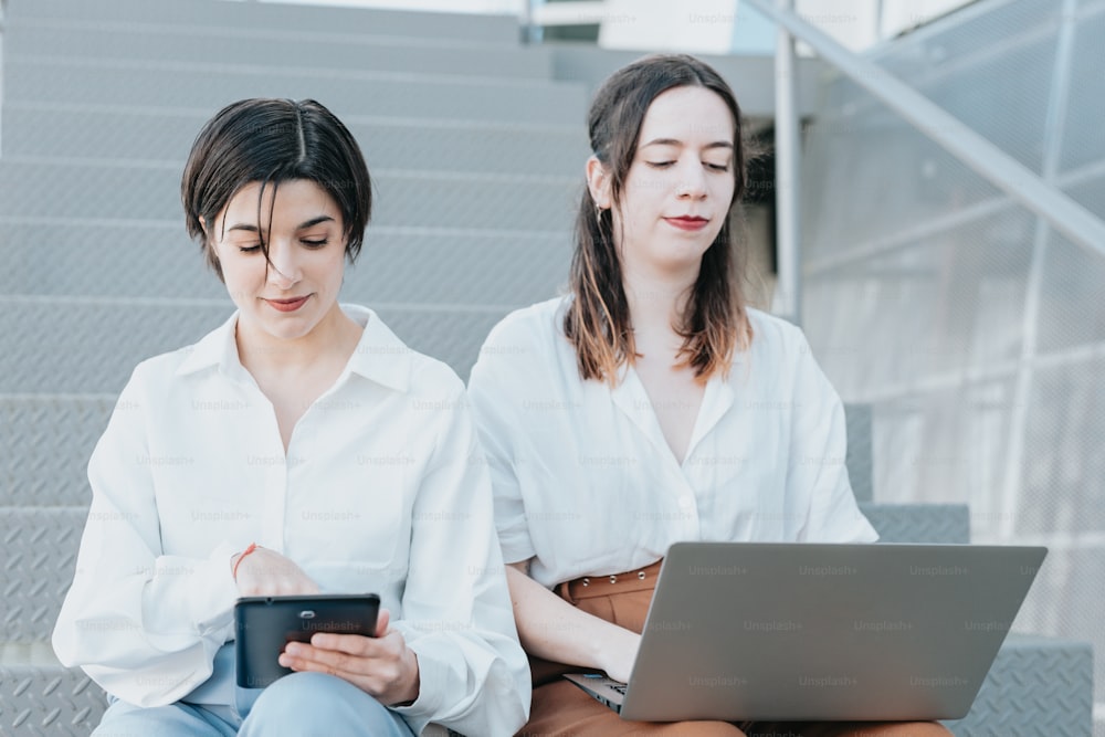 duas mulheres sentadas nos degraus olhando para um laptop