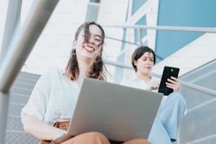 two young women sitting on steps using a laptop computer