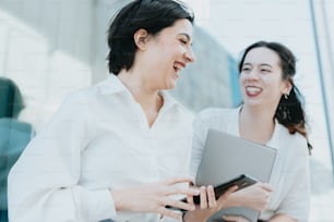 two women laughing and holding a tablet computer