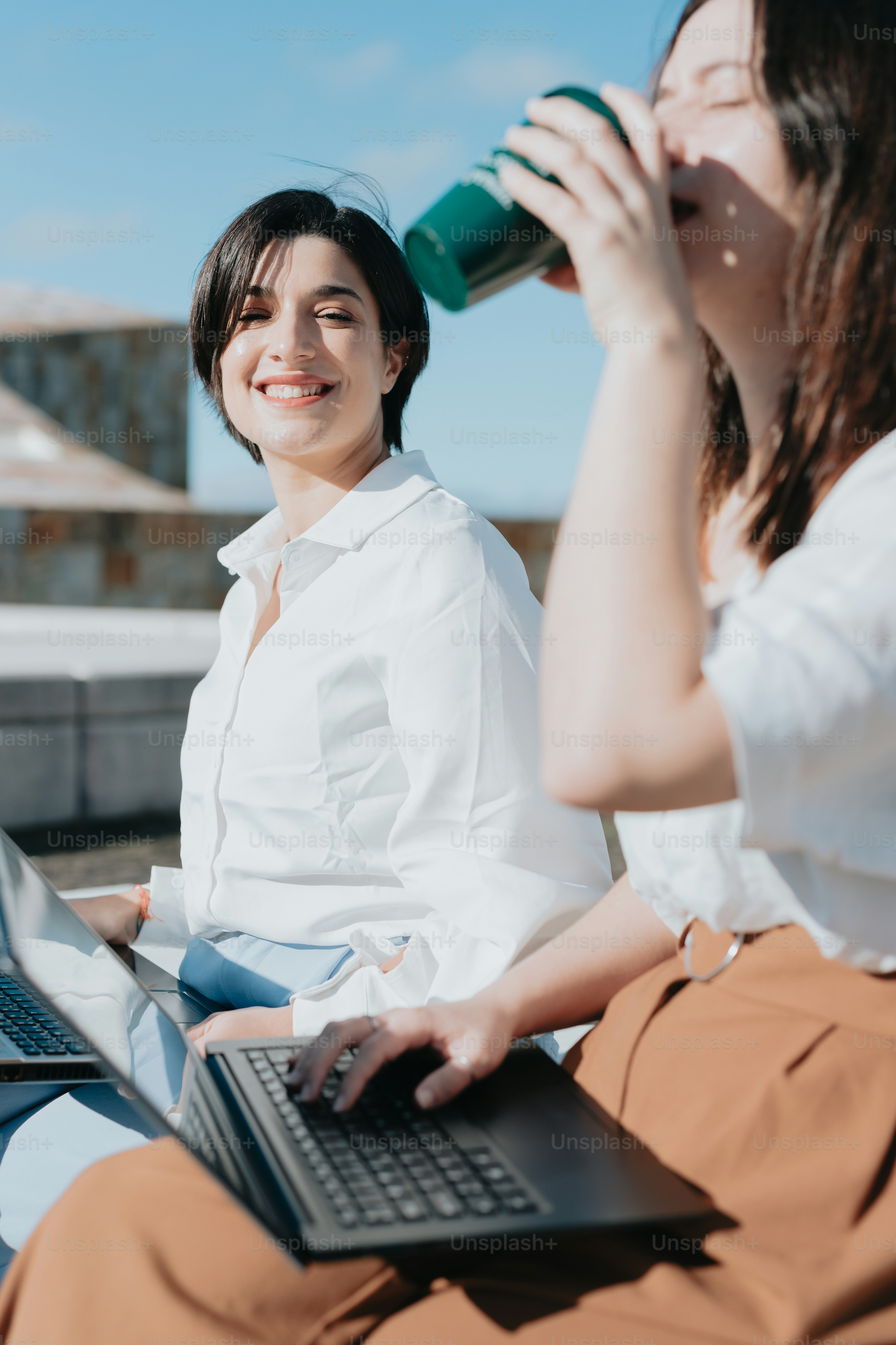 Due donne sedute a terra con computer portatili