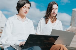 a couple of women sitting next to each other on top of a laptop computer