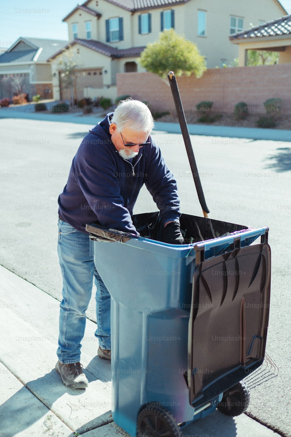 a man pushing a blue trash can down a sidewalk