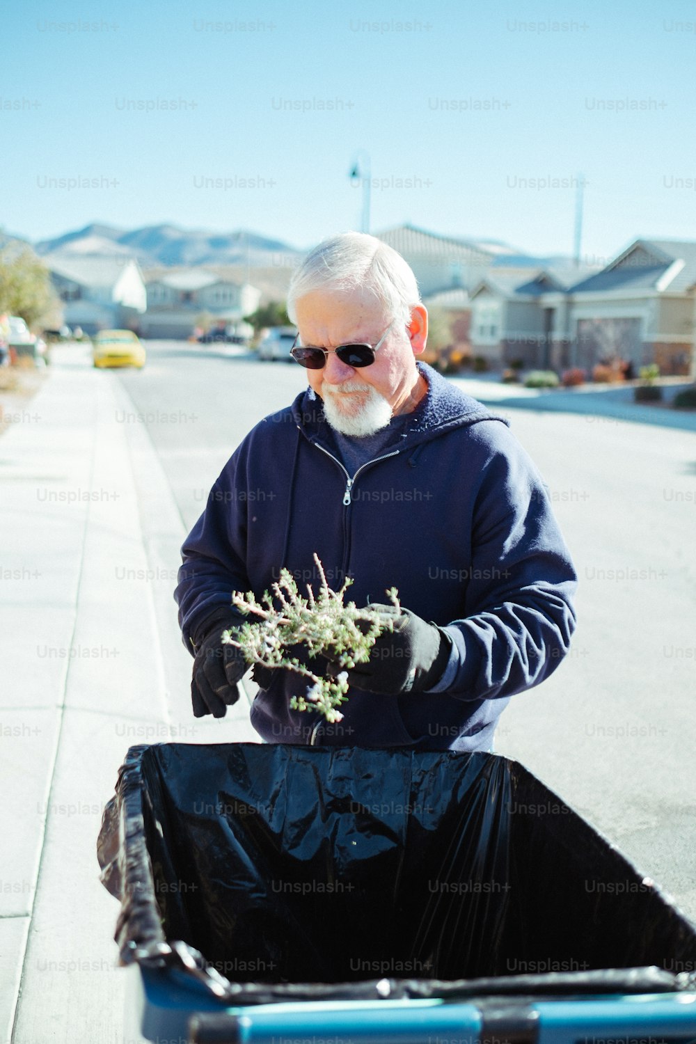 a man with a beard and sunglasses is picking up a plant from a trash can