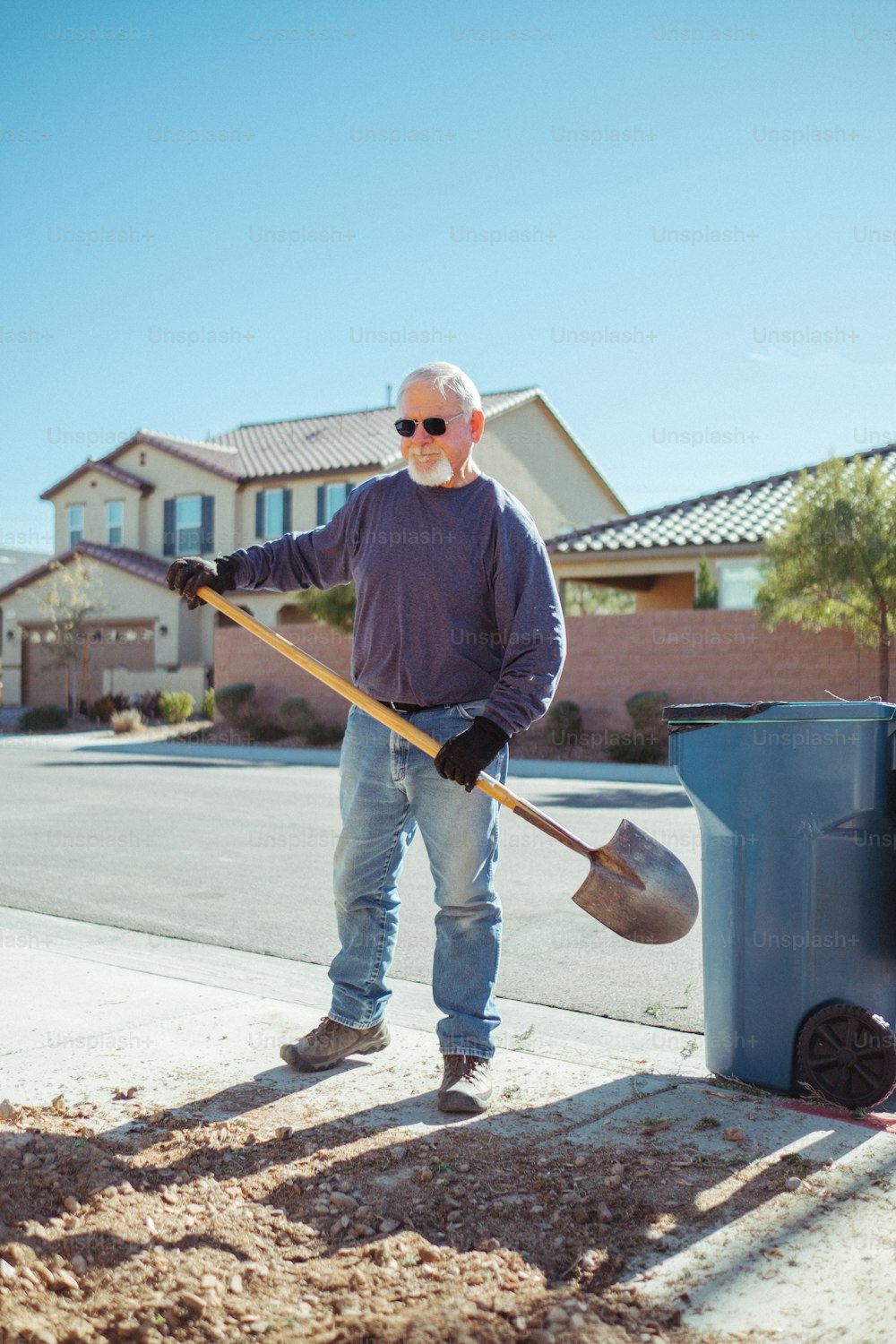 um homem de pé ao lado de uma lata de lixo segurando uma pá