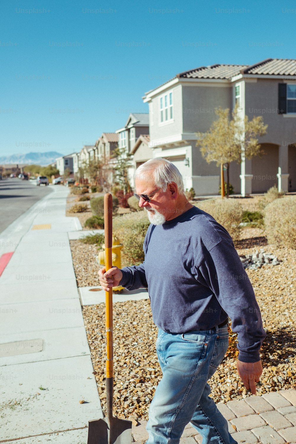 a man walking down a sidewalk with a shovel