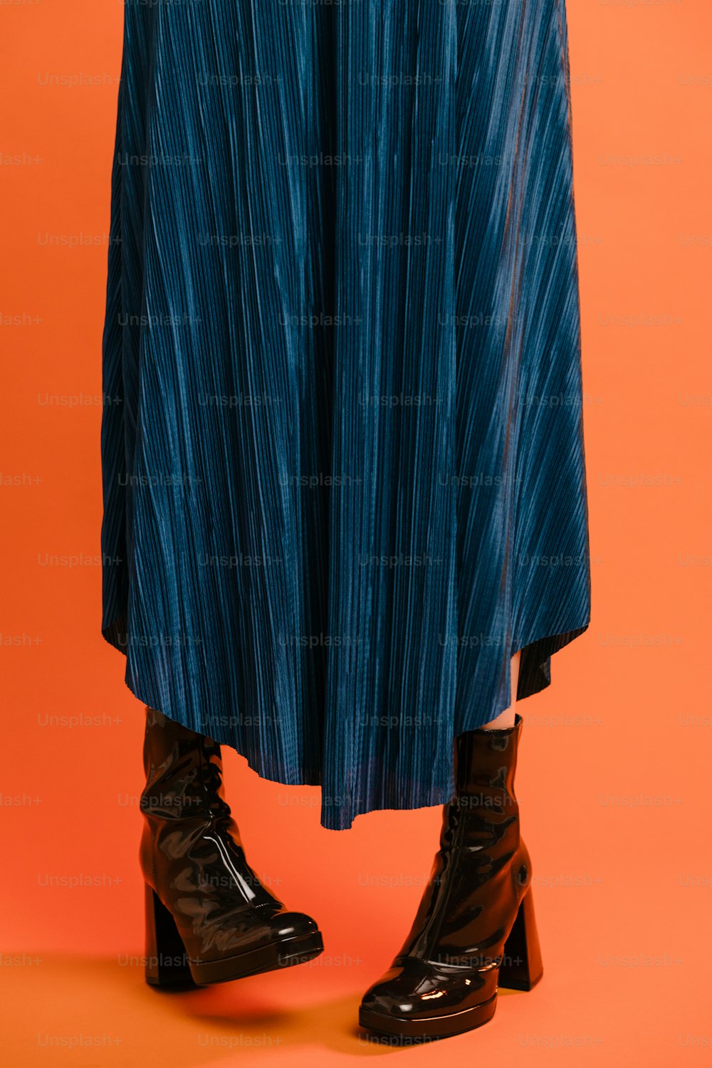 a woman wearing a blue pleated skirt and black boots
