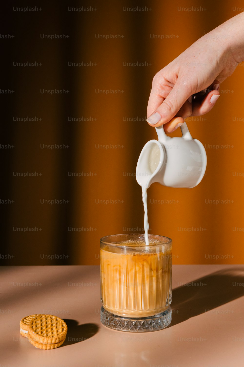 una persona vertiendo leche en un vaso con una galleta a un lado
