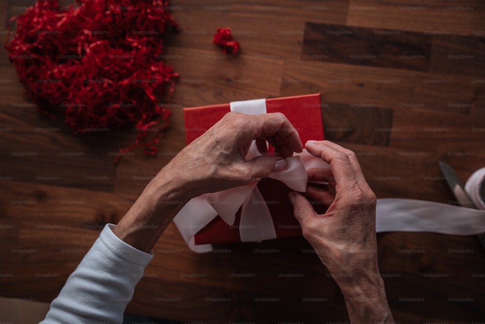 a person wrapping a red gift with white ribbon
