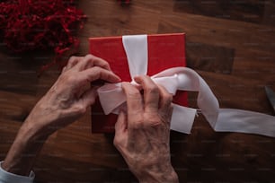 a person wrapping a red gift with white ribbon