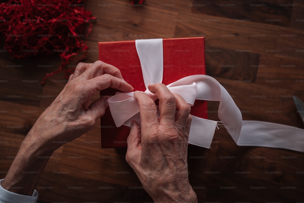 a person wrapping a red gift with white ribbon