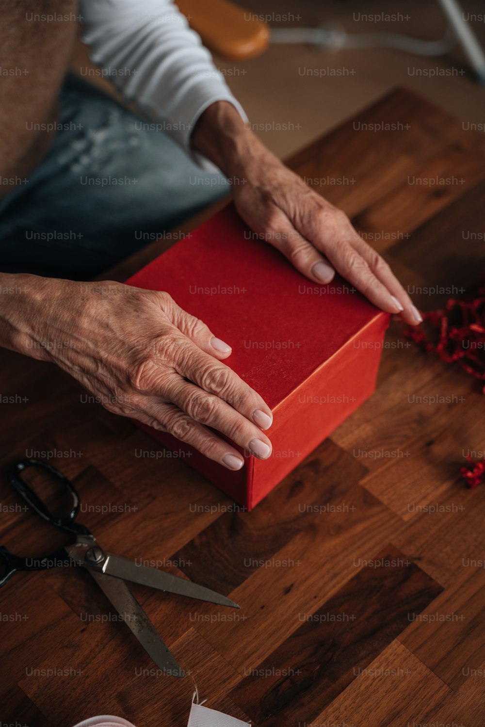 uma pessoa segurando uma caixa vermelha em cima de uma mesa de madeira