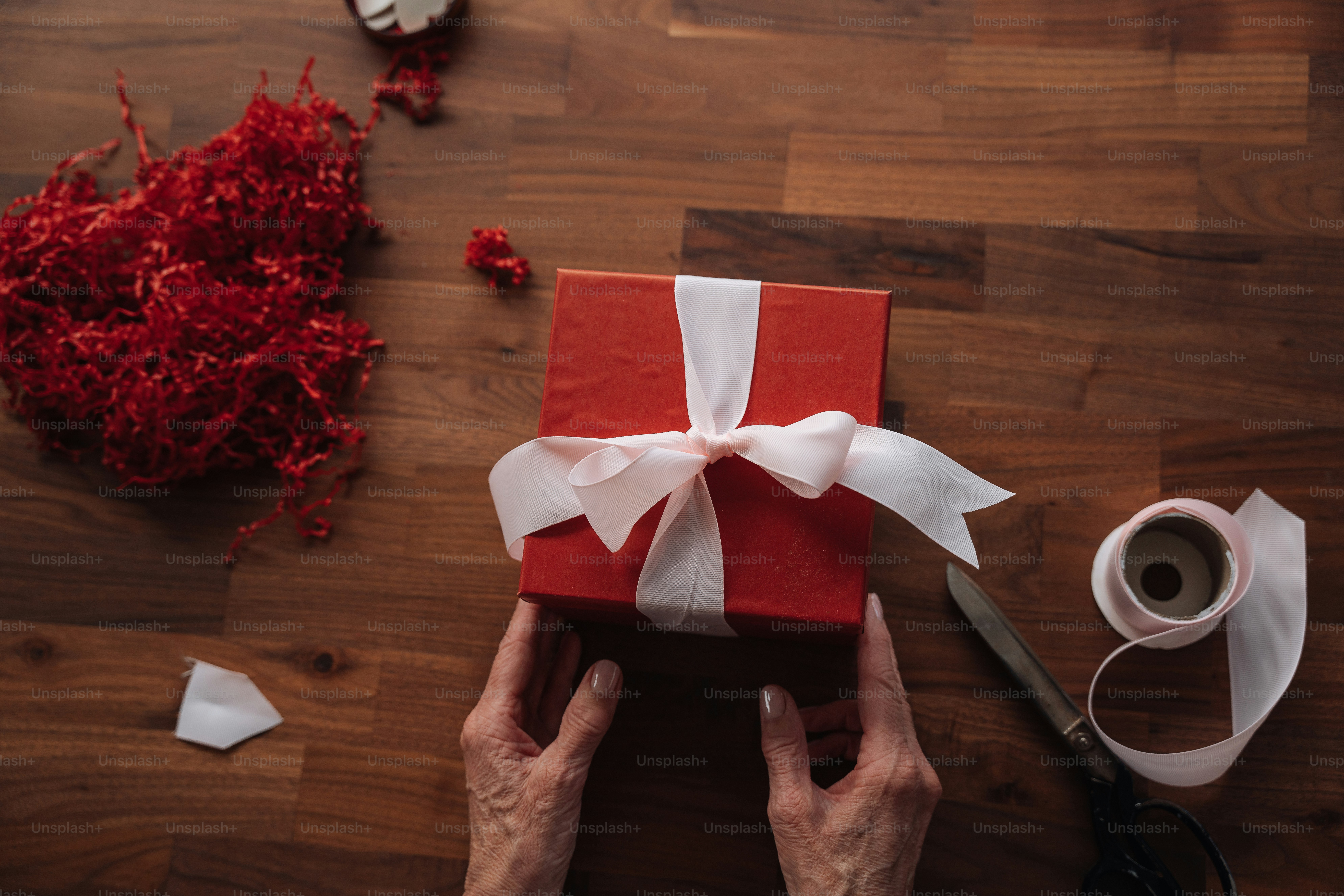 a person holding a red gift box with a white ribbon
