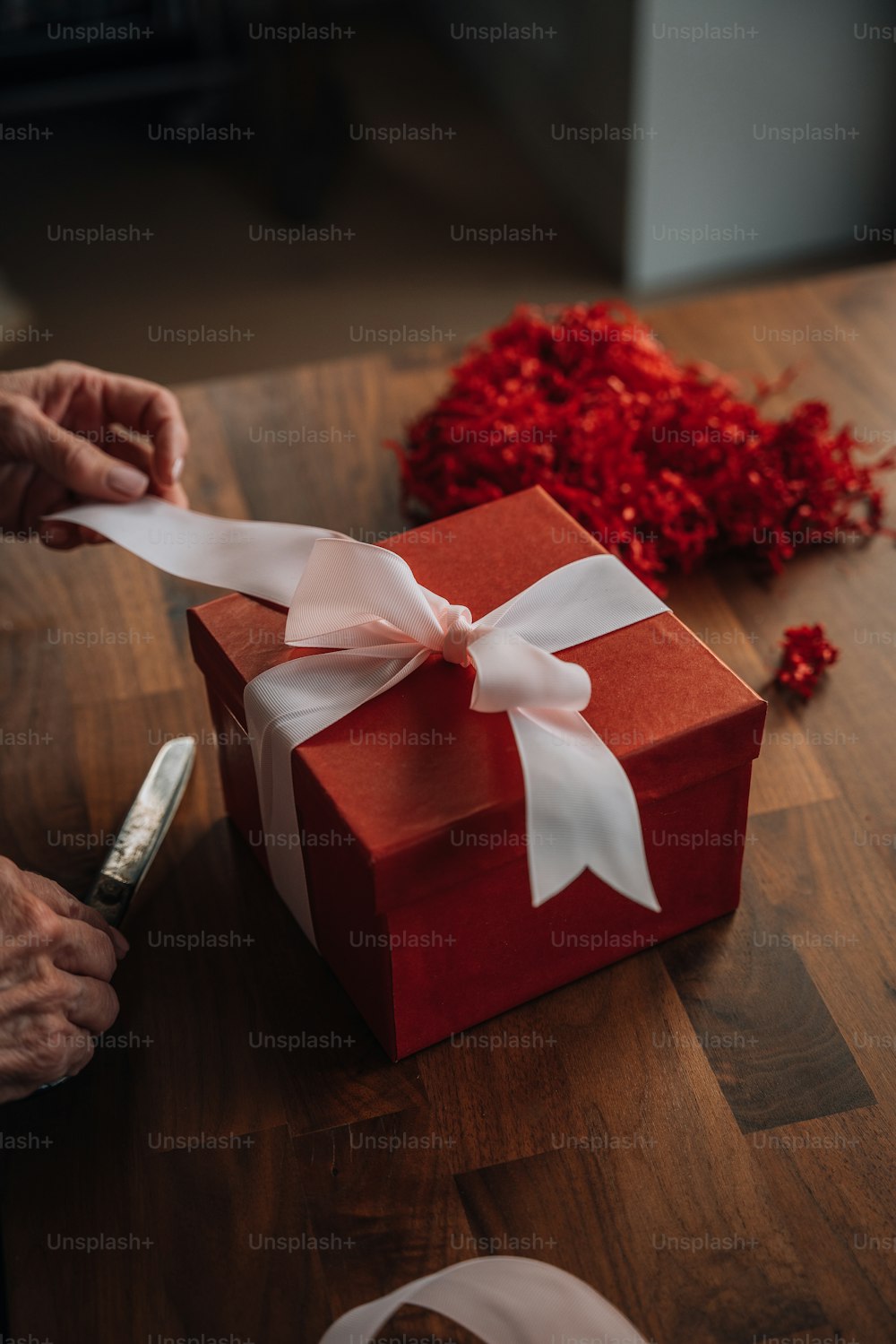 a person wrapping a red gift box with a white ribbon