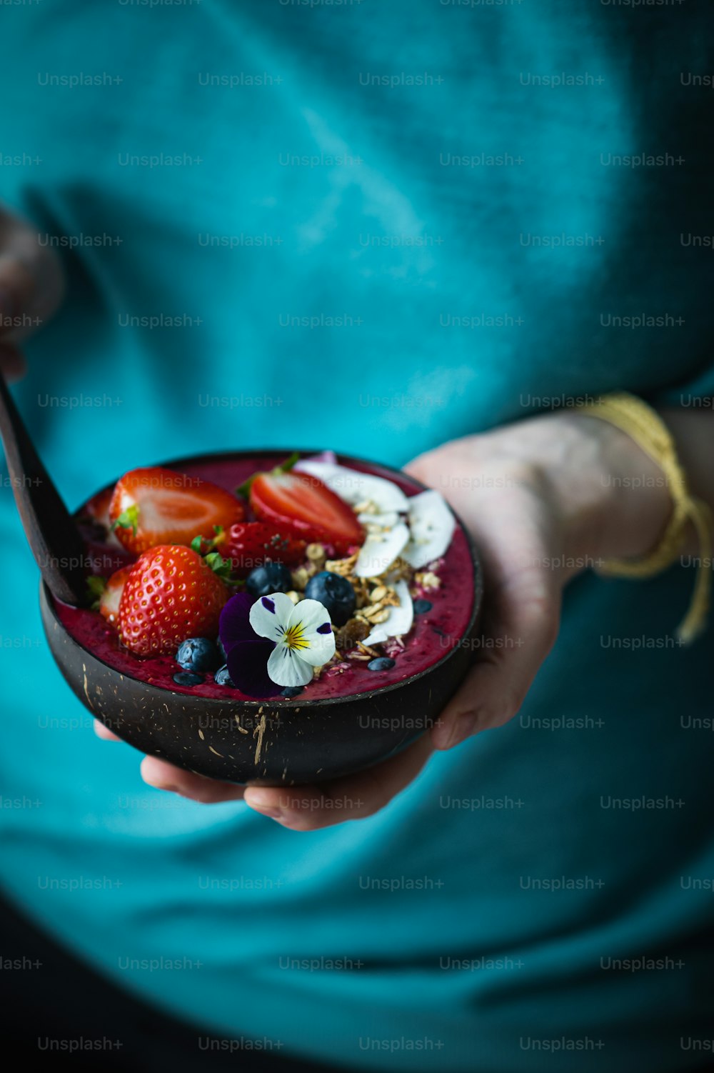 a person holding a bowl of fruit with a spoon in it