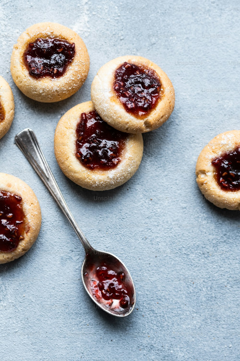 a table topped with cookies covered in jam next to a spoon
