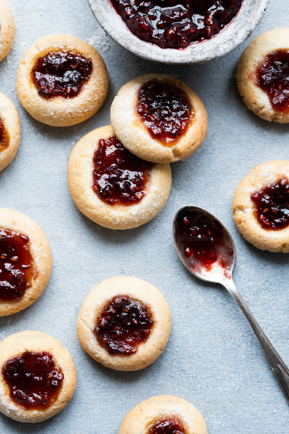 a table topped with cookies covered in jam next to a bowl of jelly