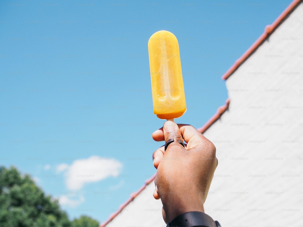 a hand holding an orange popsicle in front of a building