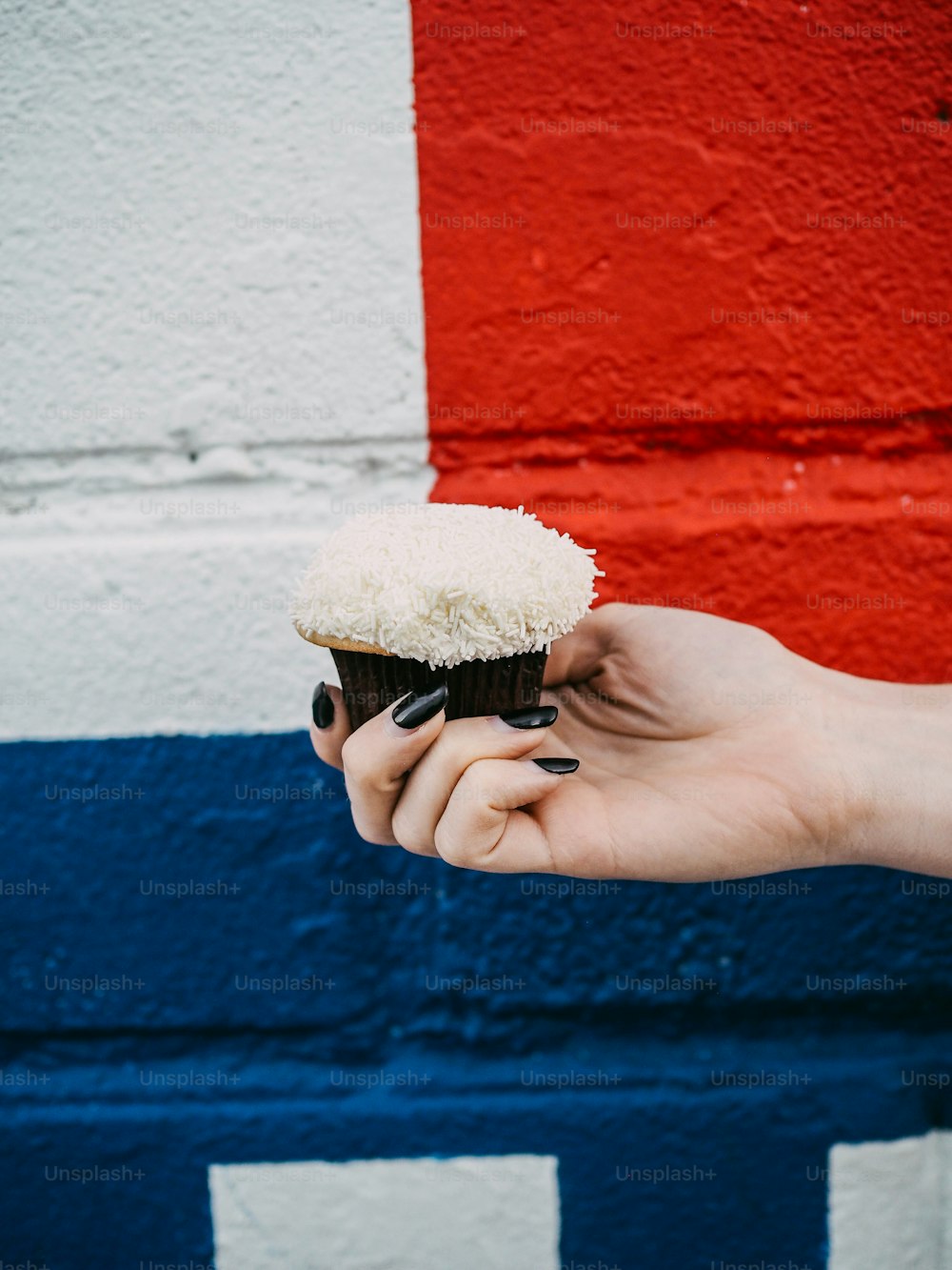 a hand holding a cupcake with white frosting
