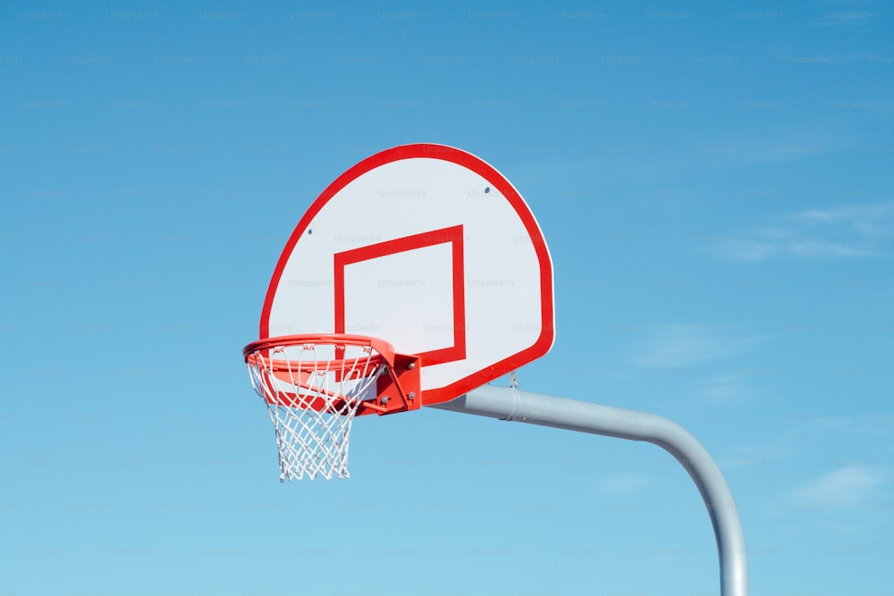 a red and white basketball hoop with a blue sky in the background