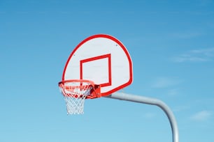 Un aro de baloncesto rojo y blanco con un cielo azul en el fondo