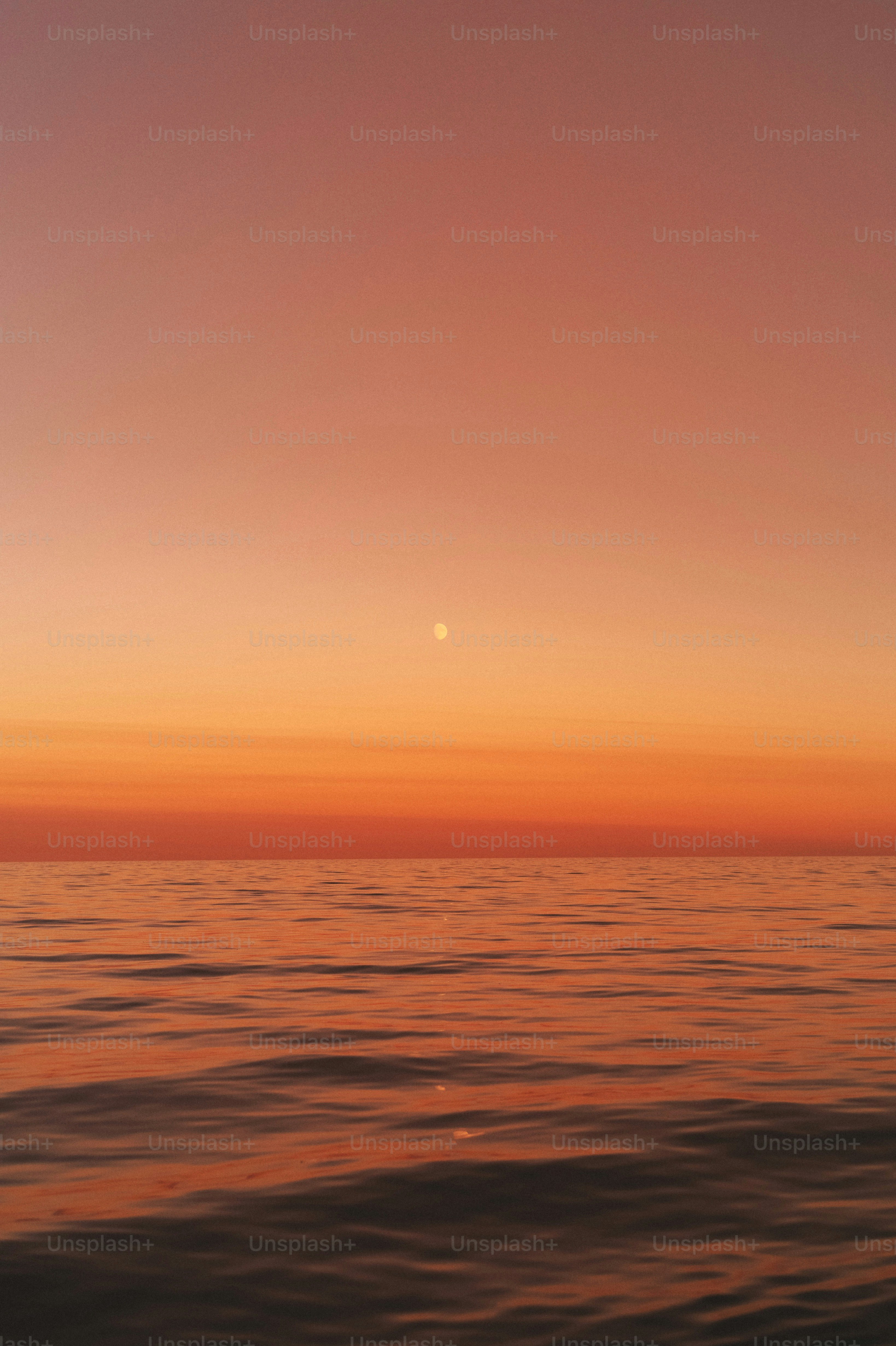 the sun is setting over the ocean with a boat in the water